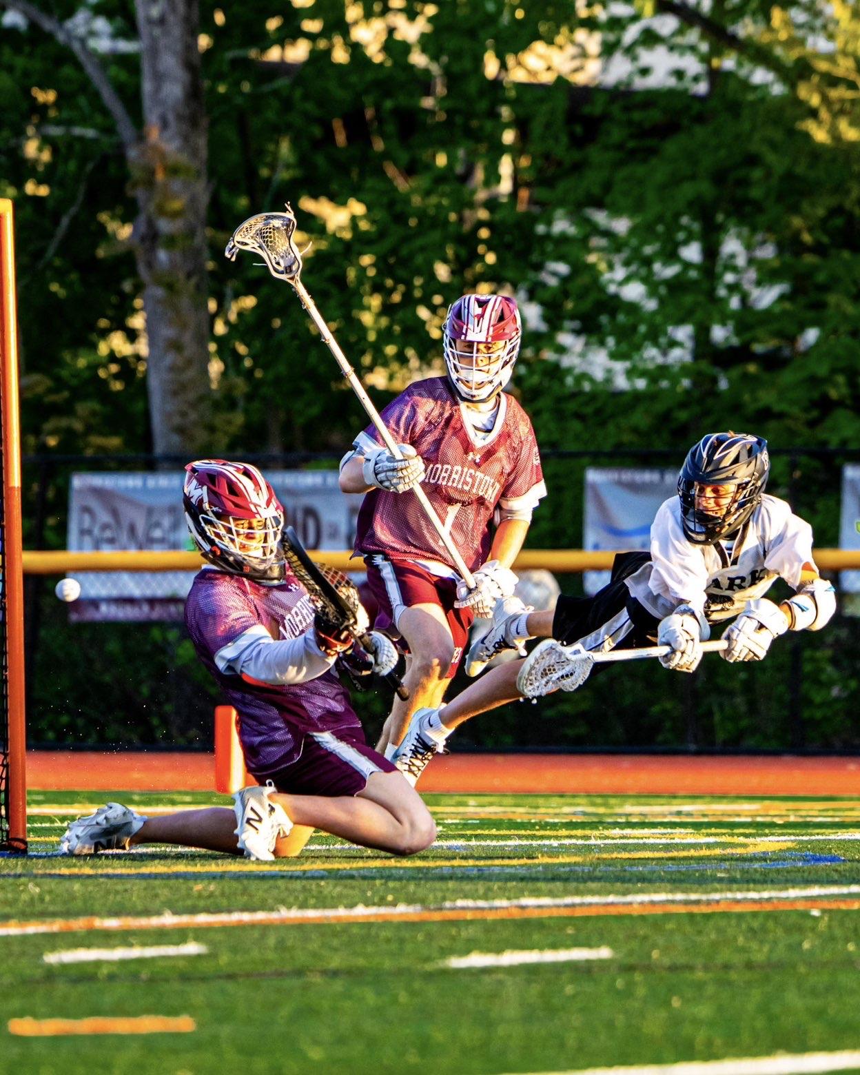 Boys lacrosse players battle for a loose ball near the crease in golden evening light